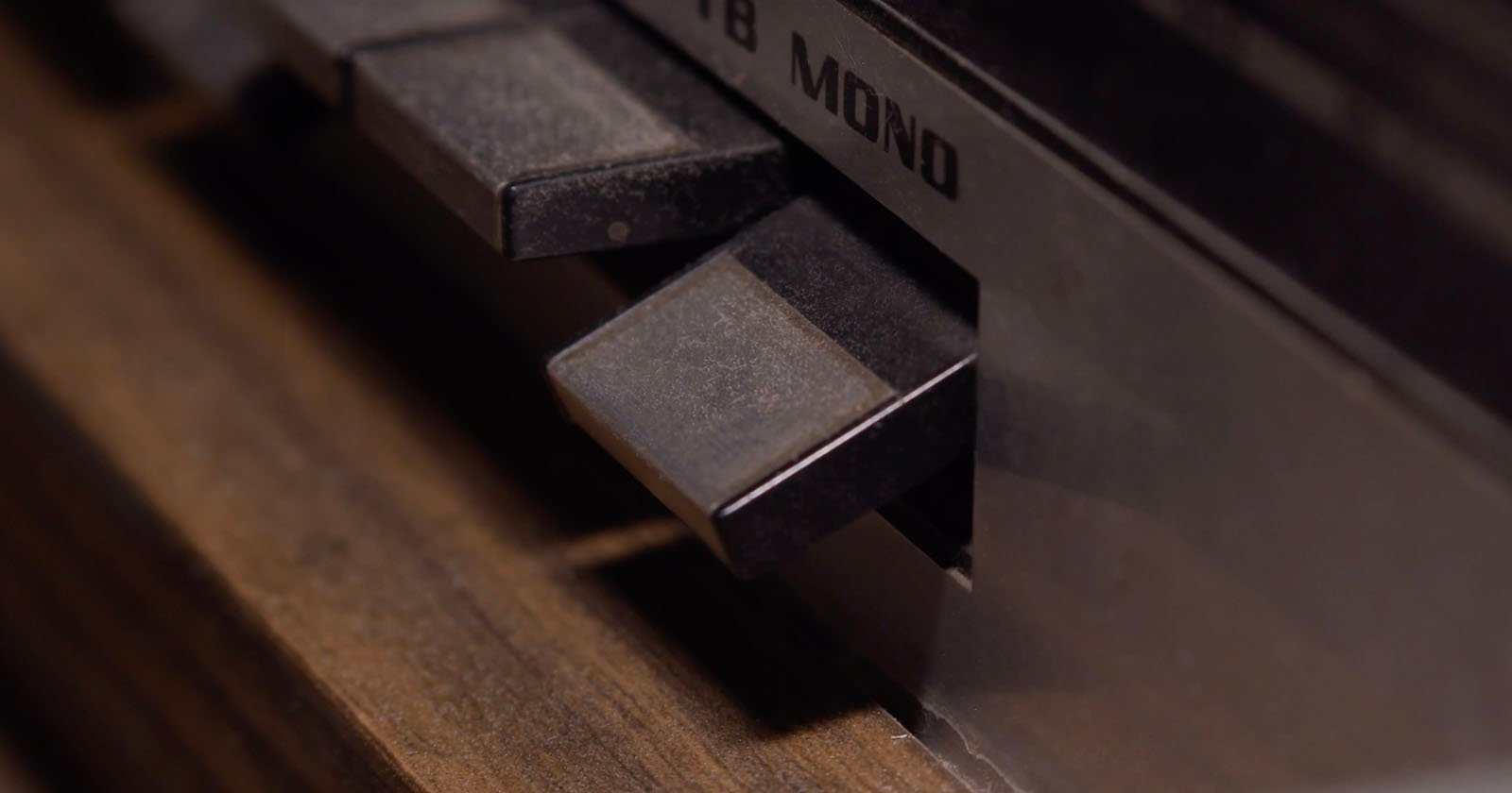Close-up of buttons on a vintage audio device showing a “MONO” label, with dark, rectangular buttons set against a wooden and metal surface.
