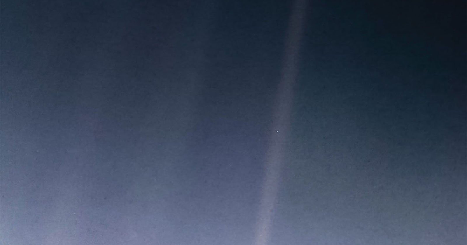 A famous photograph of Earth from a great distance, with the planet appearing as a tiny pale dot against a vast, dark background of space, intersected by bands of sunlight.