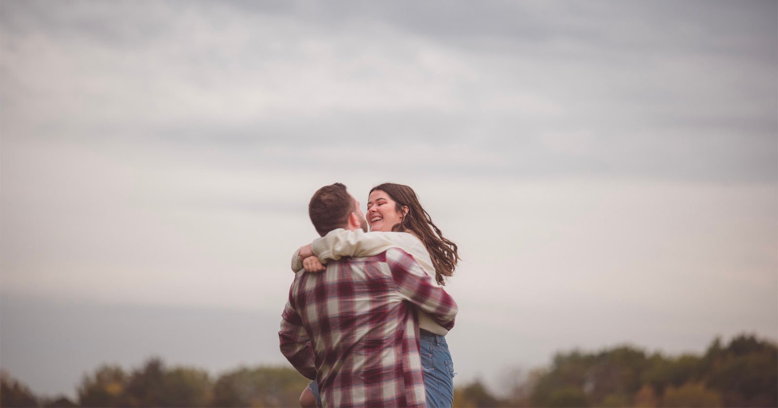 A couple hugs with the sky in the background.