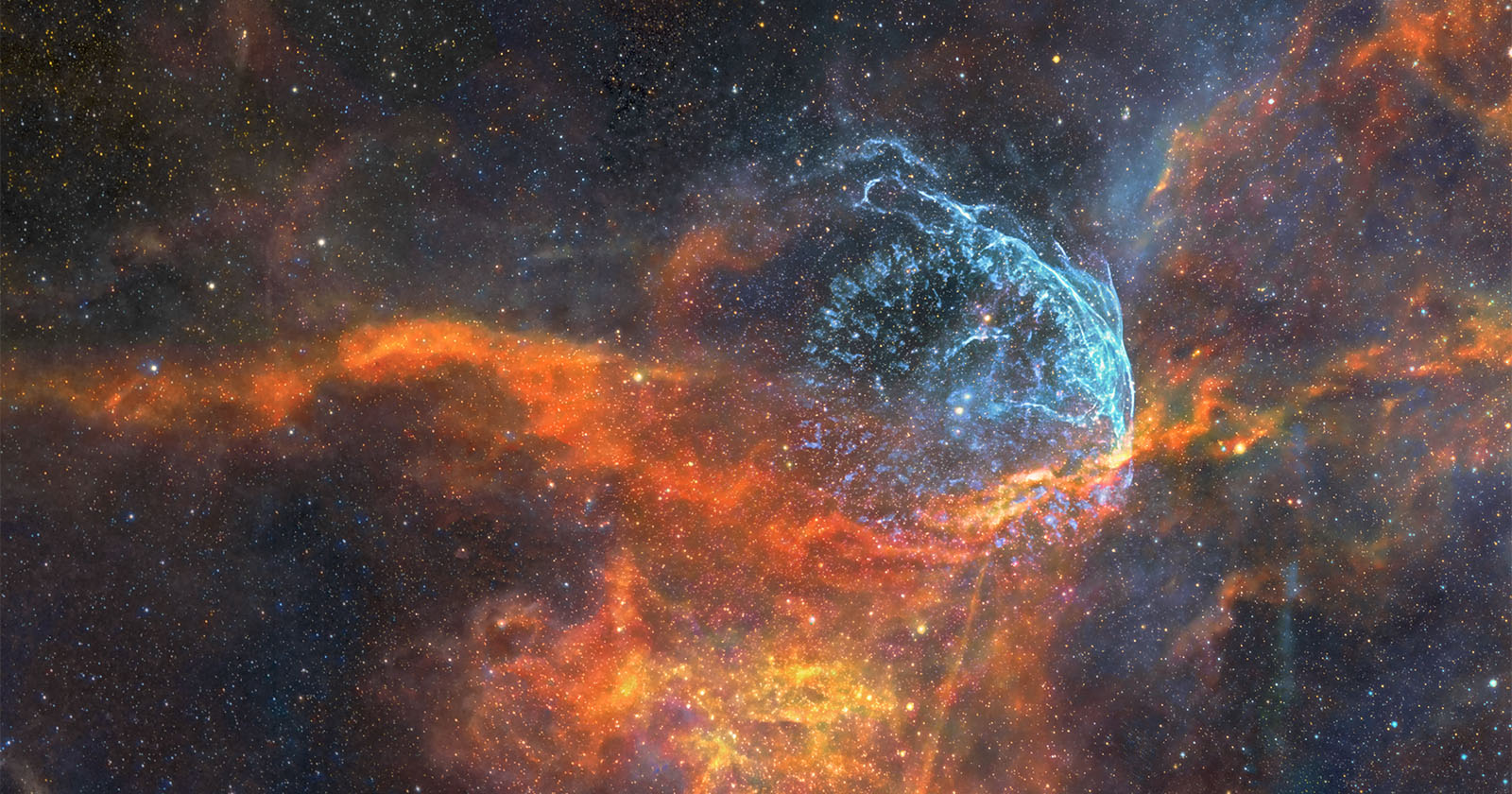A vivid image of a nebula in space, showcasing bright colors with swirling patterns. Orange and red clouds contrast against a dark background, with a striking blue formation resembling a gaseous arc. Twinkling stars are scattered throughout.
