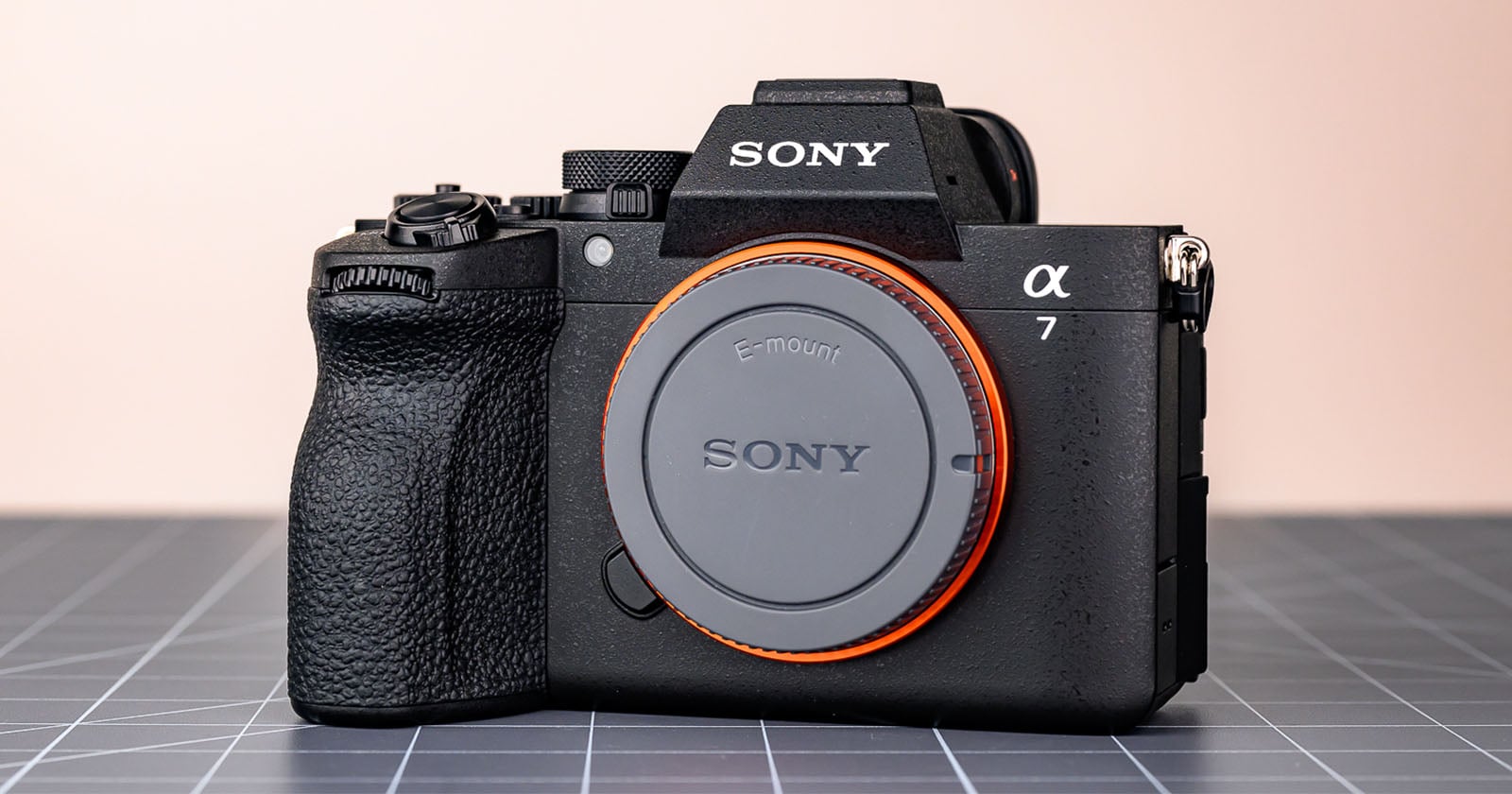 A Sony Alpha 7 mirrorless digital camera body with an E-mount cap, shown on a grid-patterned surface against a plain, light-colored background.