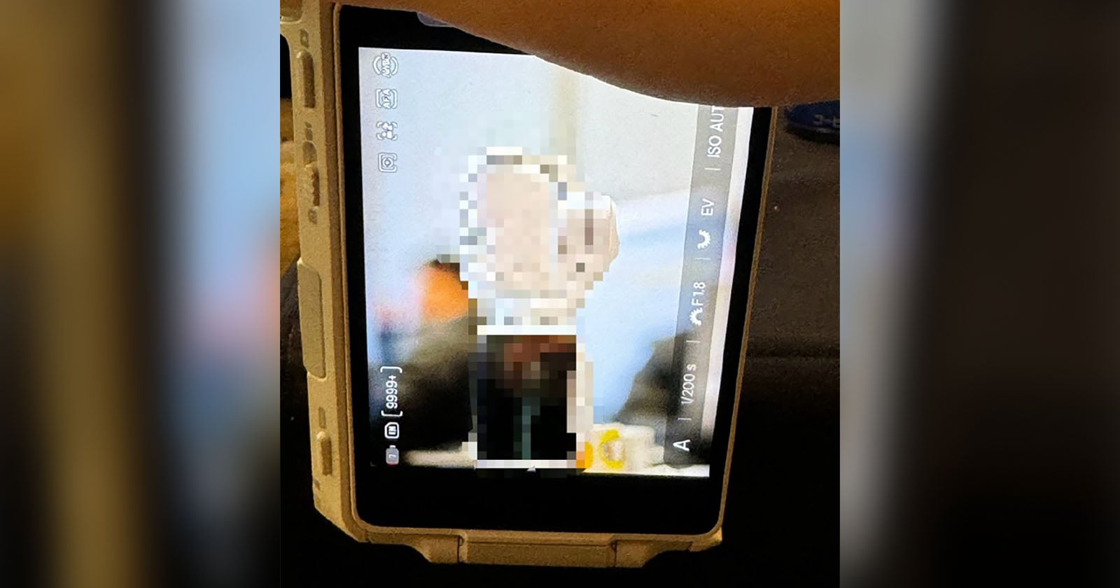 A close-up of a digital camera screen shows a blurred photo being reviewed, with camera settings and icons visible on the display and a hand partly visible at the top.