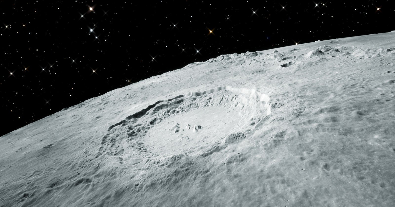 A detailed view of the moon’s surface shows a large, prominent crater surrounded by rough, uneven terrain. The dark, star-filled expanse of space forms the backdrop, highlighting the crater's stark, shadowed features and the rugged lunar landscape.