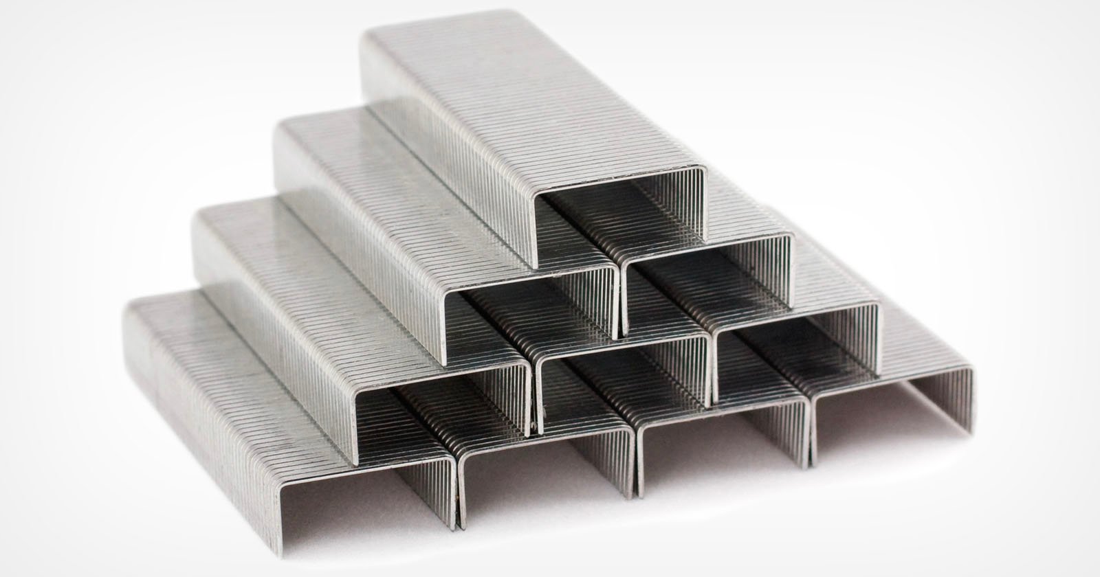 A stack of metal staples arranged in a pyramid shape on a white background.