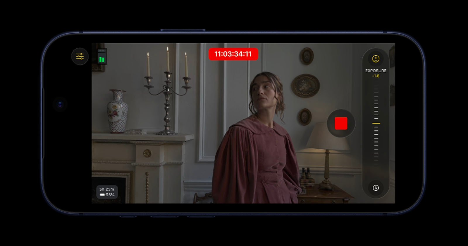 A smartphone screen displays a video recording interface with a woman in a historic-style dress standing near a fireplace, decorative vases, and candlesticks in a vintage room. Exposure settings and a red record button are visible.