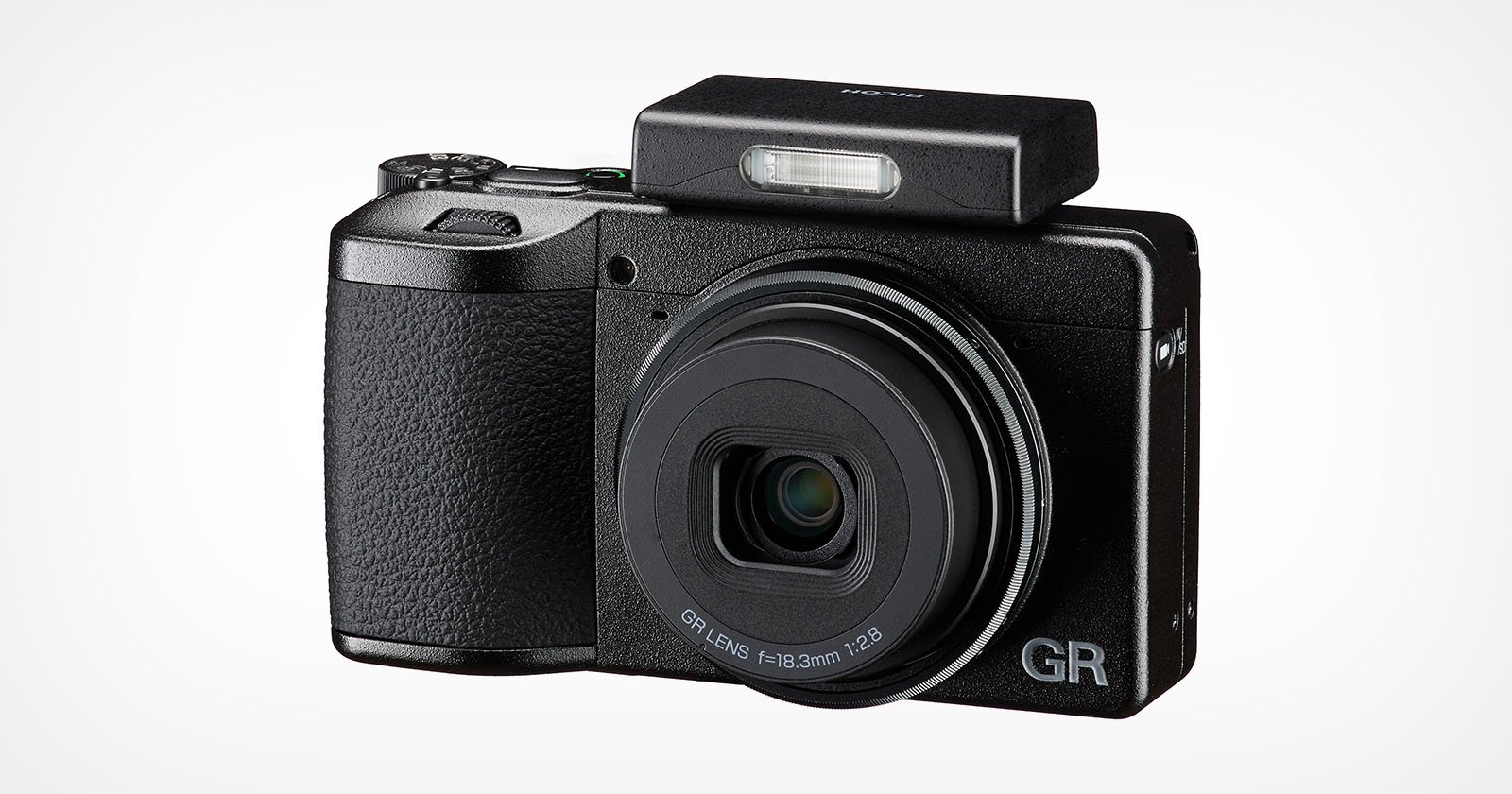 A compact black digital camera with a textured grip, extended lens, and raised rectangular pop-up flash. The letters GR are visible on the lower right corner of the camera front.