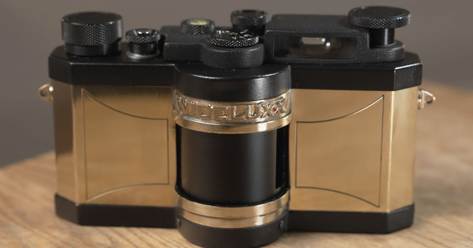 A close-up of a vintage camera with gold and black detailing, labeled WIDELUX on a central band, resting on a wooden surface.