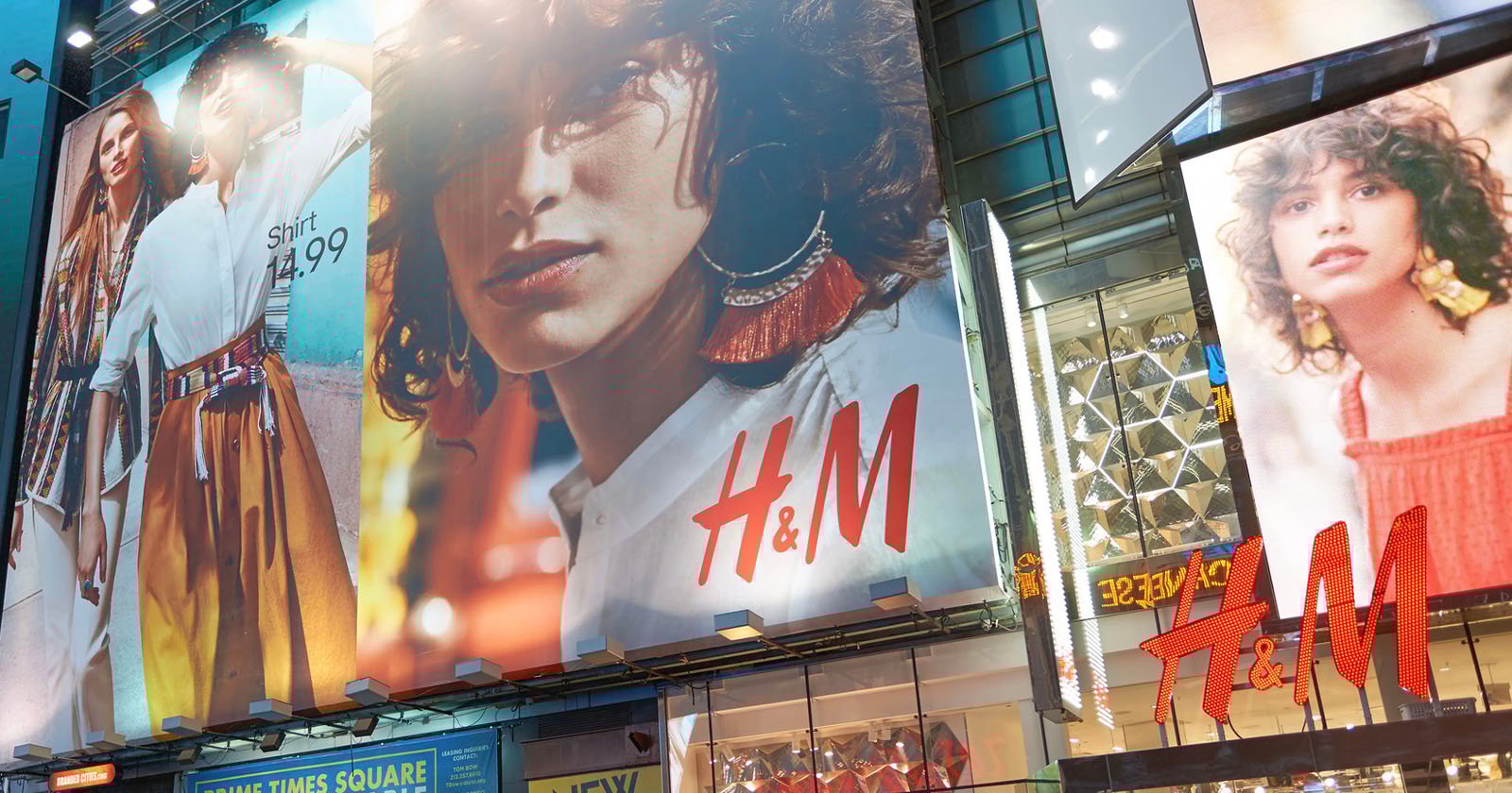 Advertising billboards on a building facade display enlarged fashion images, including people modeling clothing and accessories. The H&M logo is prominently featured. The building is located in a bustling urban area.