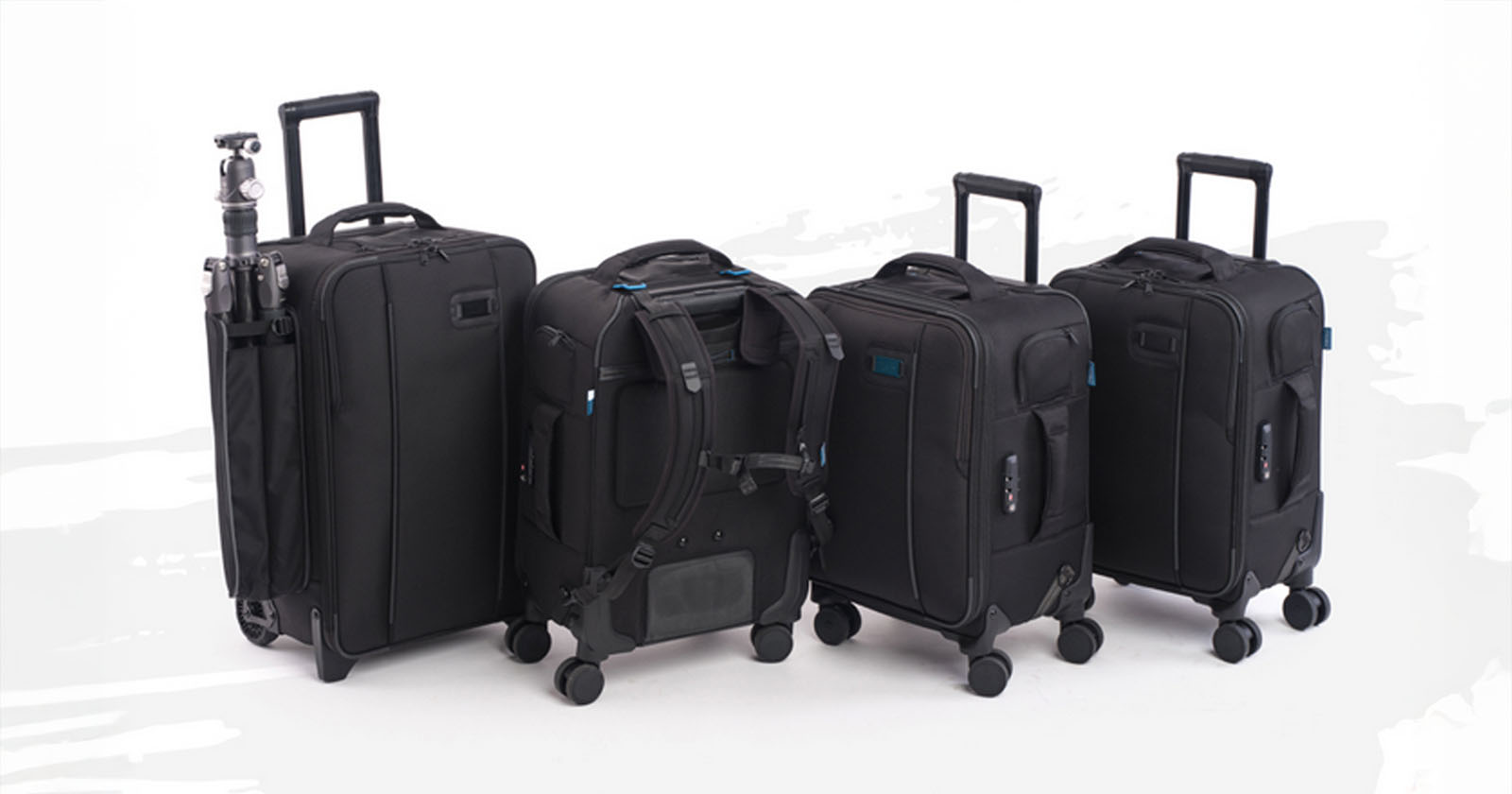 Four black rolling suitcases stand side by side on a white background; one has a tripod attached, and another is shown with backpack straps visible.