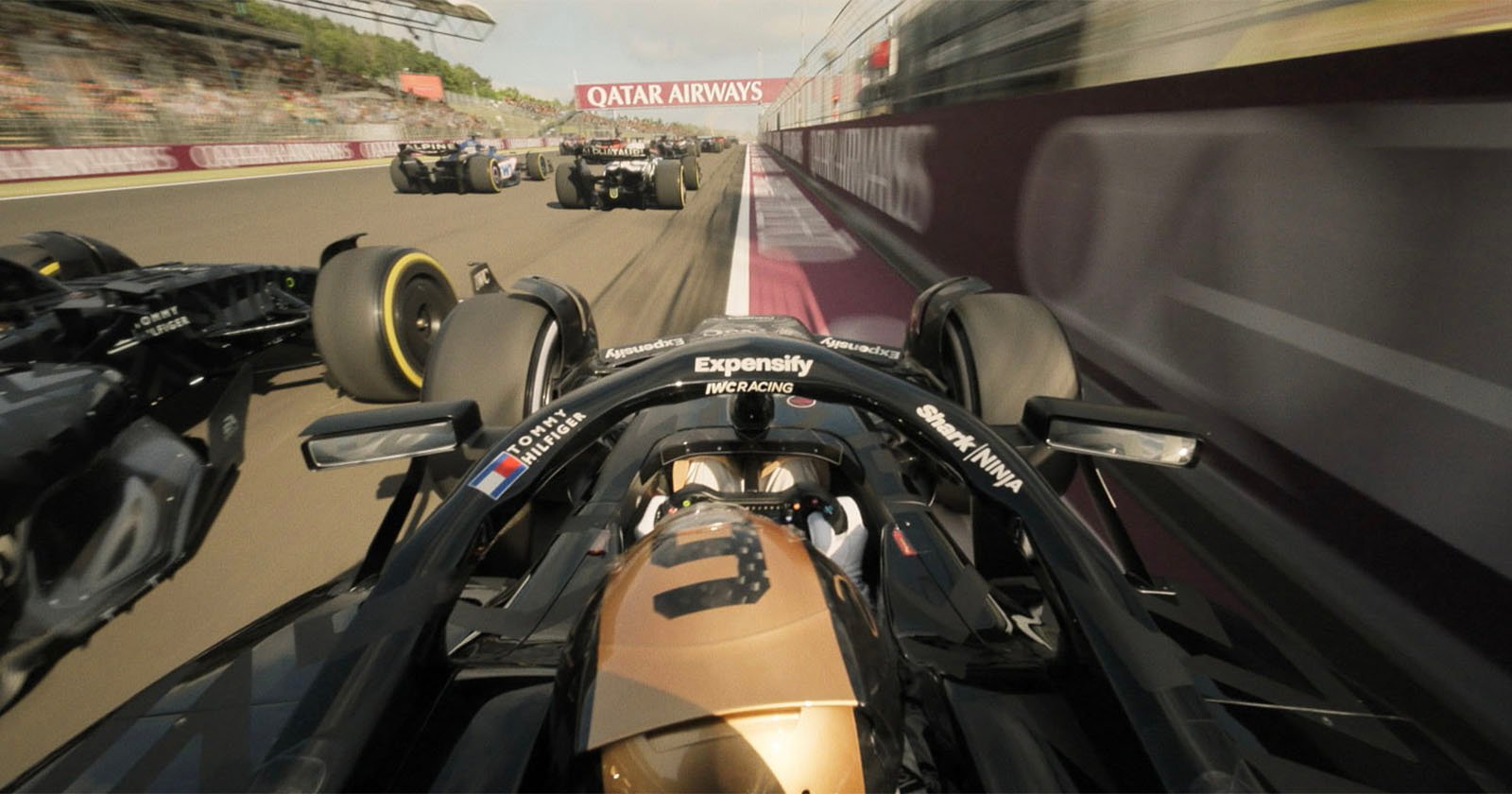 Onboard view from a black and gold Formula 1 car racing alongside several other cars on a track, with Qatar Airways banner visible above. The scene captures high speed and intense competition.