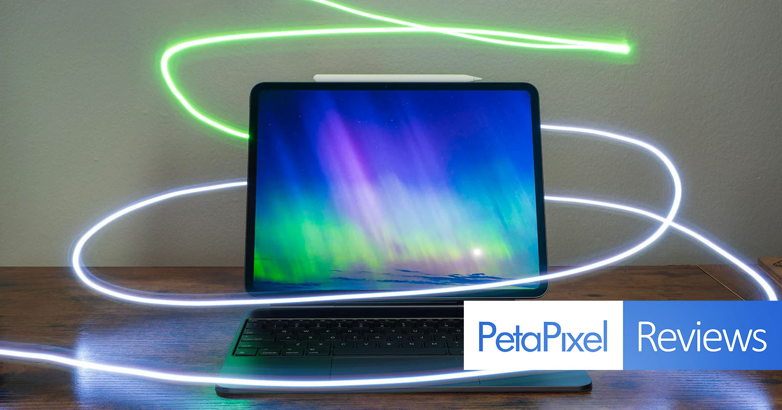 A sleek tablet with a keyboard attachment displays a vibrant, colorful aurora on the screen. Light trails surround the device, adding a dynamic effect. The Petapixel logo and the word Reviews are visible in the bottom right corner.