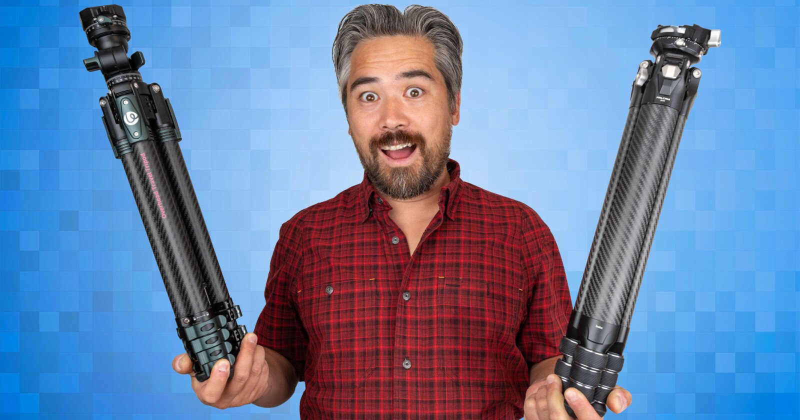 A man in a red plaid shirt stands in front of a blue pixelated background, smiling and holding a tripod in each hand.