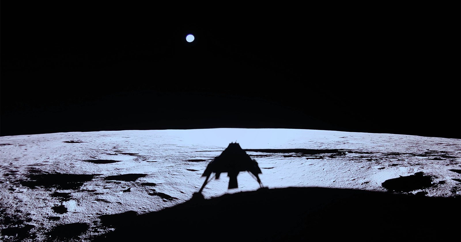 A silhouetted lunar lander is casting a shadow on the moon's surface, which appears illuminated against the dark sky. A small, bright Earth is visible in the background.