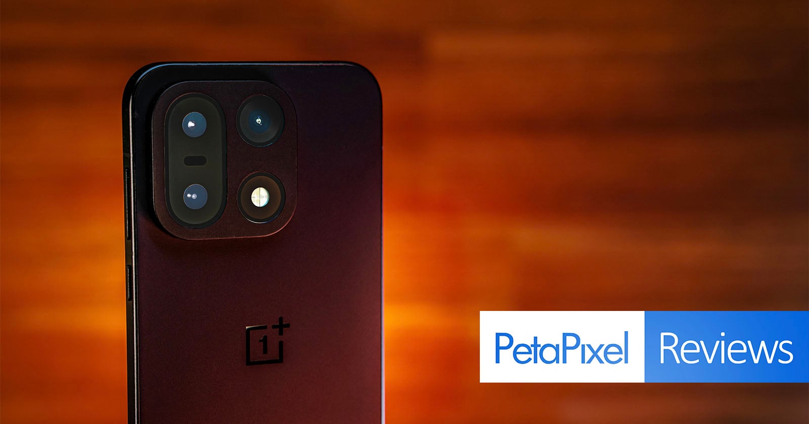 A close-up of a OnePlus smartphone’s rear camera module against a warm, blurred background, with PetaPixel Reviews text in a blue and white banner in the lower-right corner.
