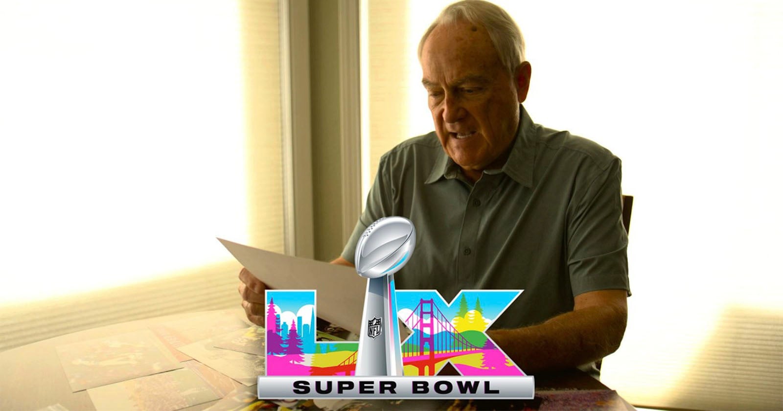 An older man sits at a table holding papers. The Super Bowl LIX logo, featuring colorful city imagery and a silver trophy, is digitally placed in the foreground. Bright light shines through windows behind him.