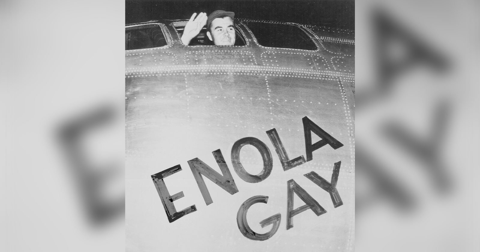 A man waves from the cockpit window of an airplane. The nose of the plane has the name Enola Gay painted in bold letters. The image is black and white, capturing a moment of historical significance.