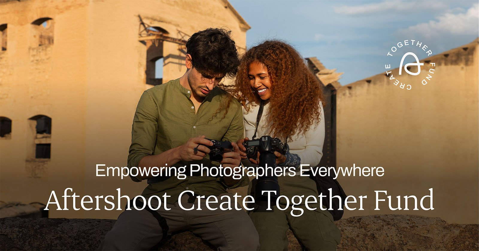A man and a woman smile and look at the screens of the cameras they are holding. They are outdoors with a building in the background. Text reads, Empowering Photographers Everywhere. Aftershoot Create Together Fund. The Aftershoot logo is in the top right corner.