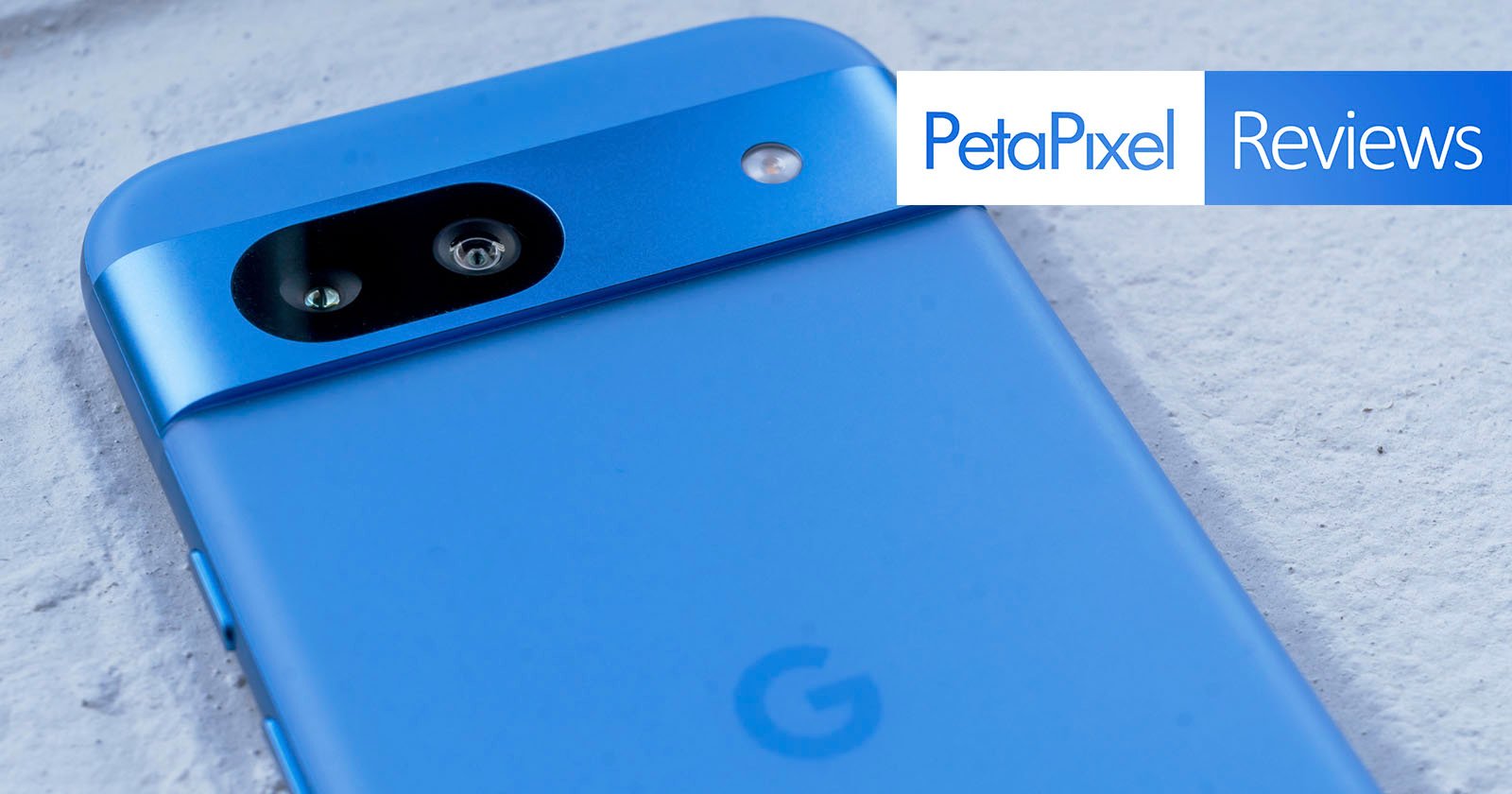 Close-up of a blue smartphone with a minimalist design showing its back camera on a white surface. There is a PetaPixel Reviews logo in the top right corner.