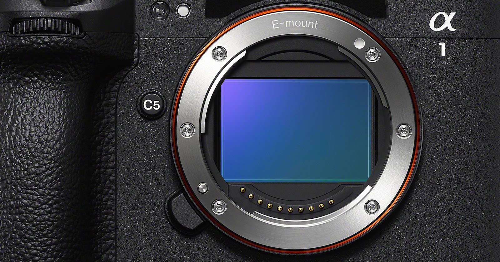 Close-up of a camera's sensor and lens mount with the label E-mount, showing a metallic circular opening and electronic contacts. The camera body has a textured black finish and visible buttons.