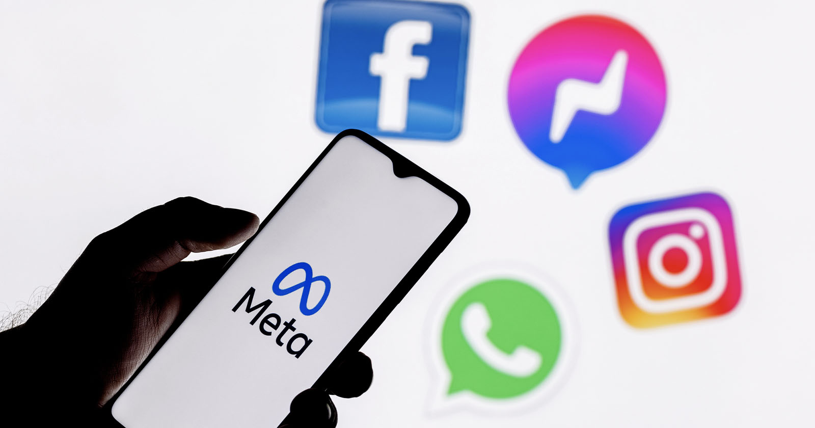 A person holds a smartphone displaying the Meta logo. In the background are social media app icons: Facebook, Messenger, Instagram, and WhatsApp, all associated with Meta. The image highlights Meta's branding and network of apps.