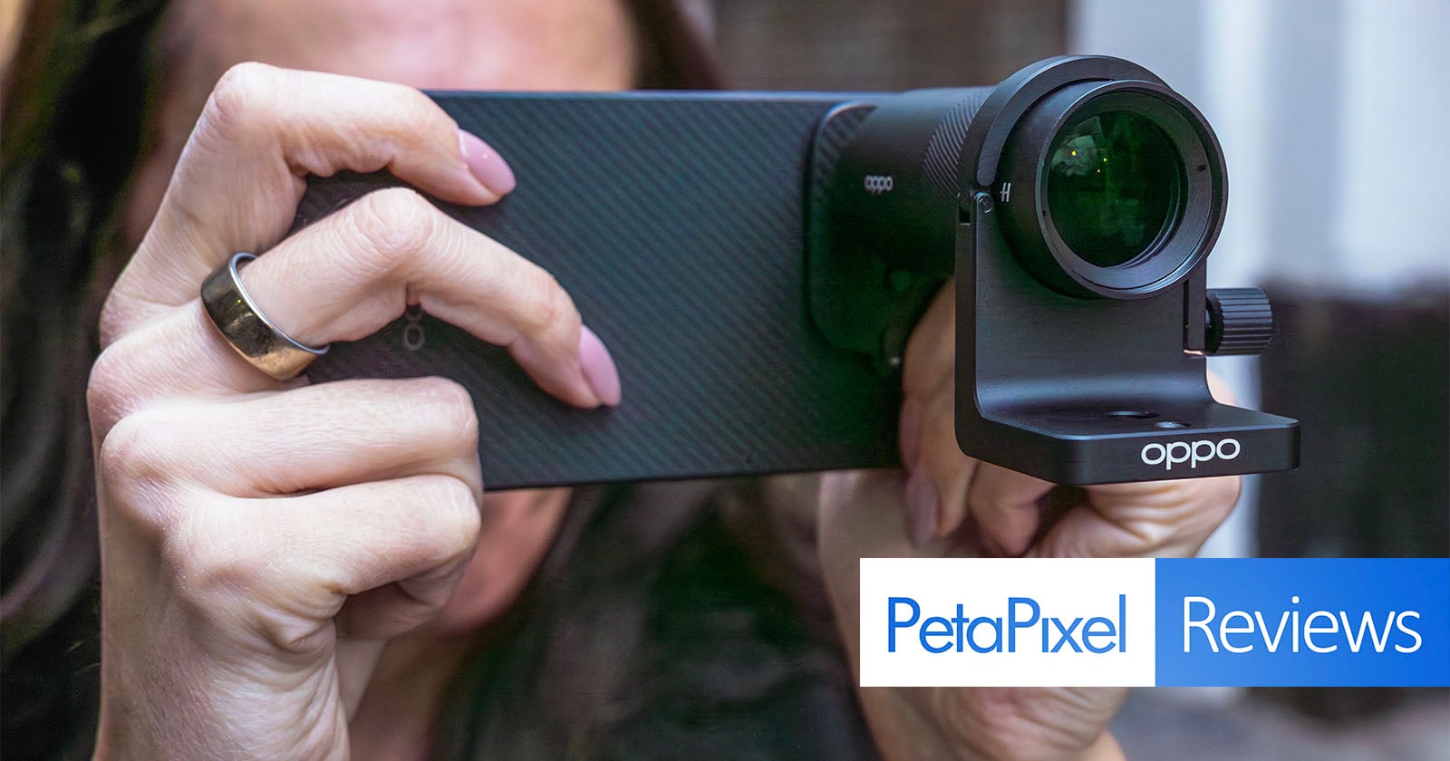 Close-up of a person holding an Oppo smartphone with an attached camera lens, preparing to take a photo. The Petapixel Reviews logo appears in the bottom right corner.
