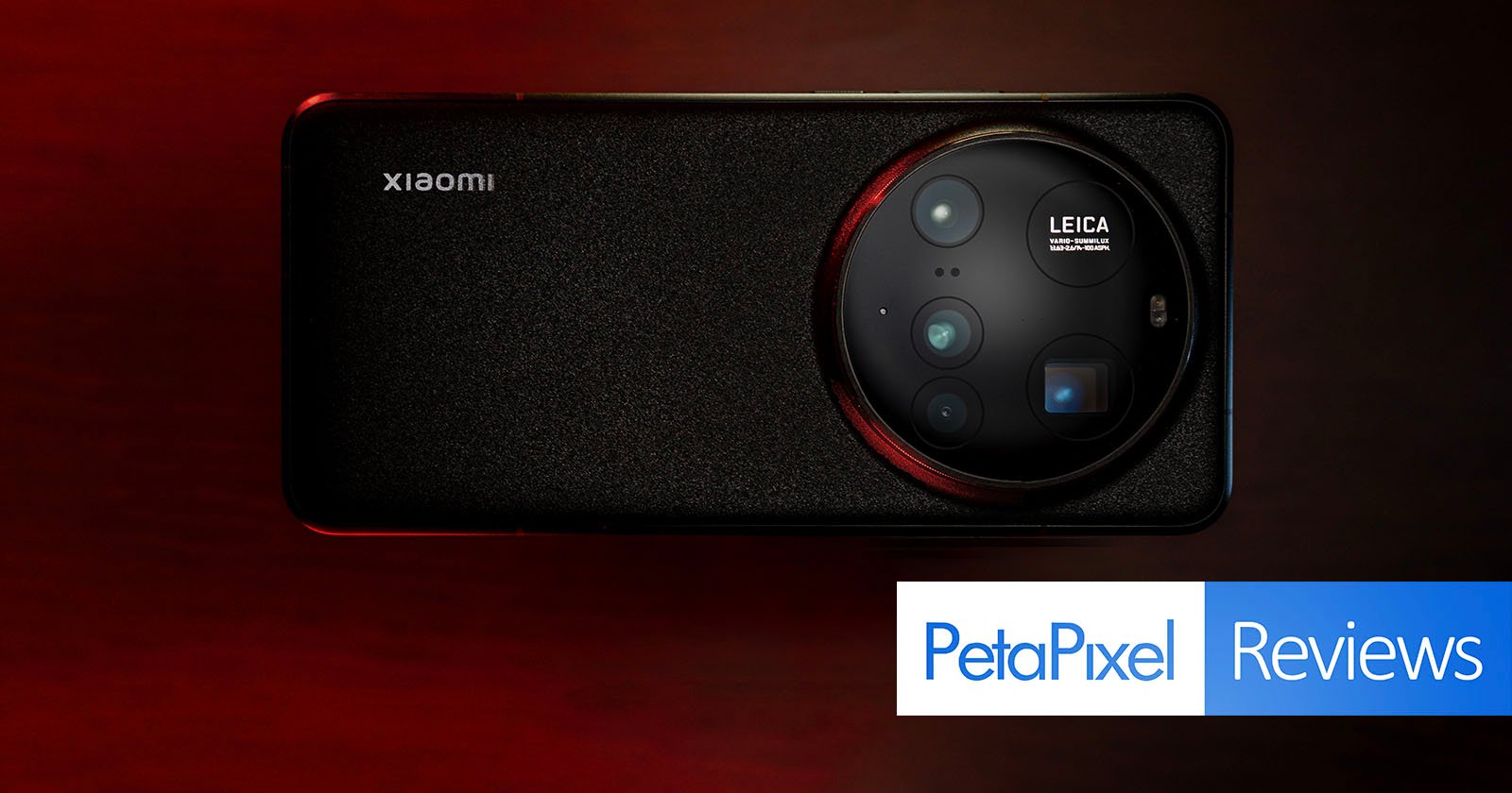 A smartphone with a large circular Leica camera module is placed on a textured surface. The phone's brand logo is visible. At the bottom right, there are graphics displaying PetaPixel Reviews with blue and white backgrounds.