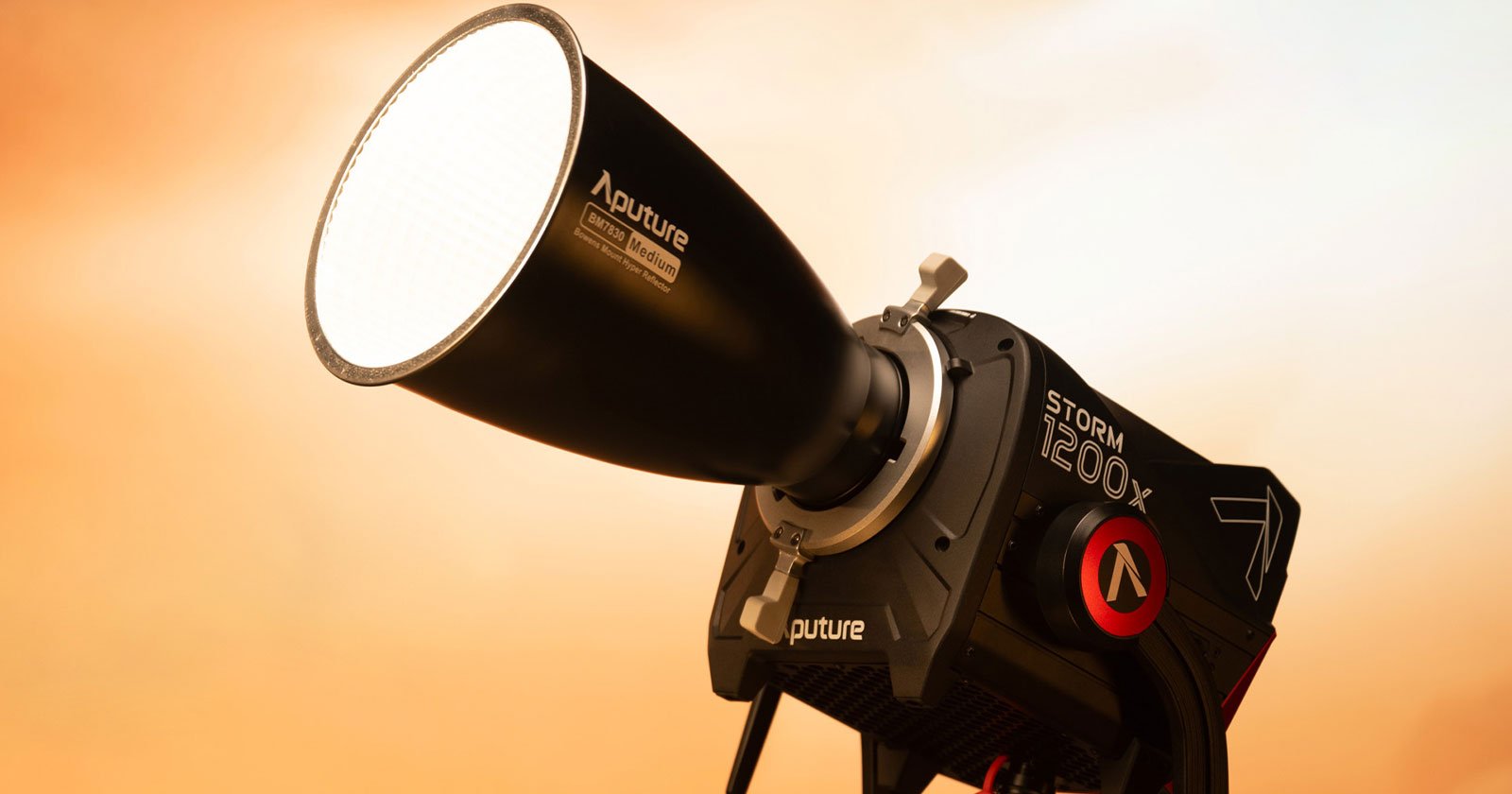 Close-up of an Aputure STORM 1200x light fixture with a bright, illuminated circular front. The light is mounted on a stand against a warm, softly blurred background, highlighting the sleek design and branding on the equipment.