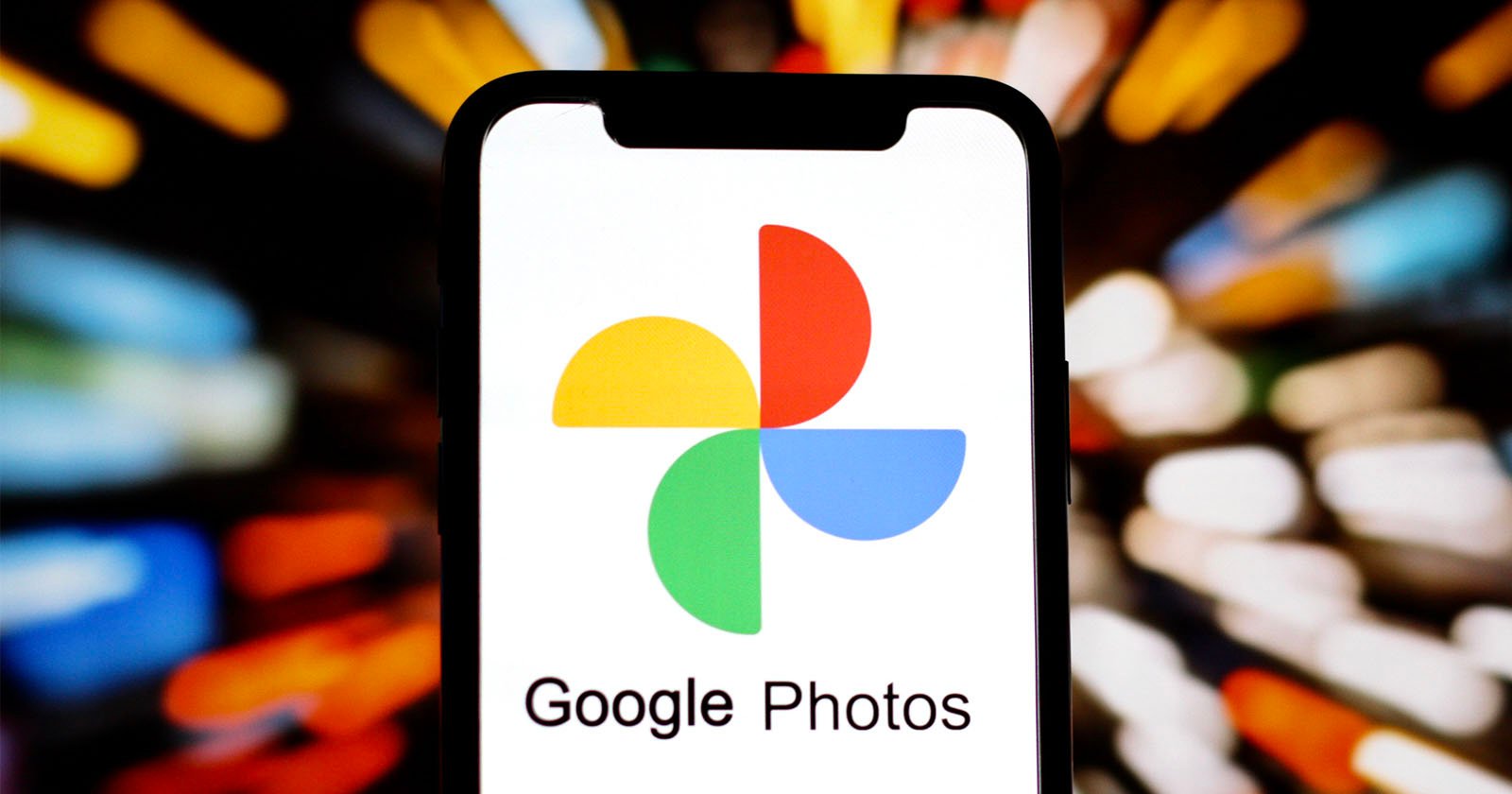 A smartphone displays the Google Photos logo and app name on its screen, with a colorful, blurred background of lights.