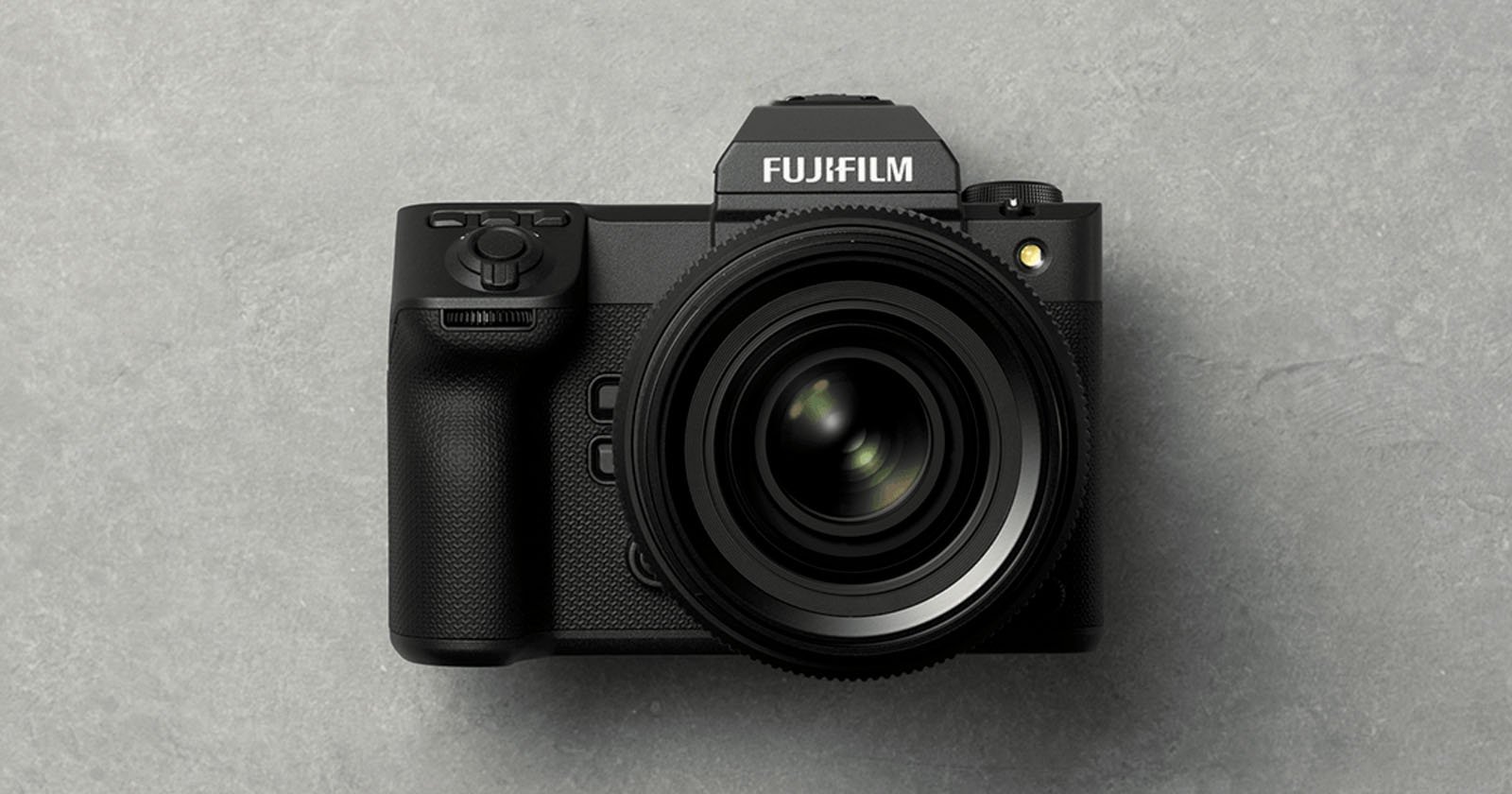 A black Fujifilm digital camera with a large lens is placed on a gray textured surface, viewed from above.