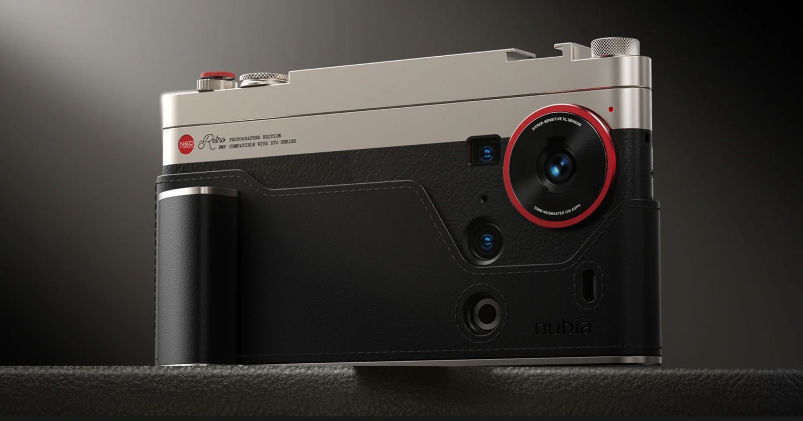 A close-up of a modern camera with a metallic top, black leather texture, and a prominent lens outlined in red. The camera has several buttons, dials, and is resting on a dark surface.