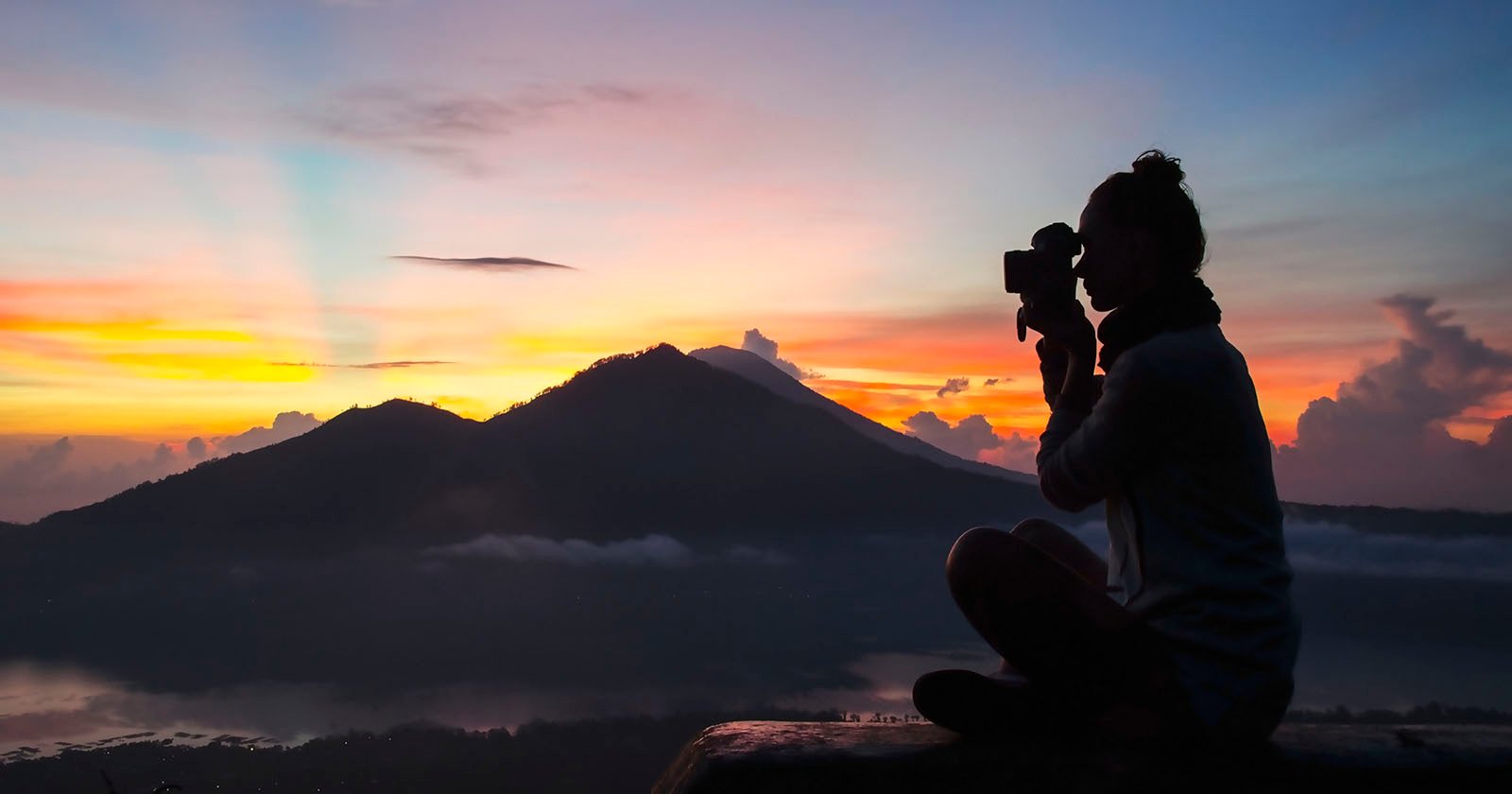 A silhouette of a women takes a photo outdoors.