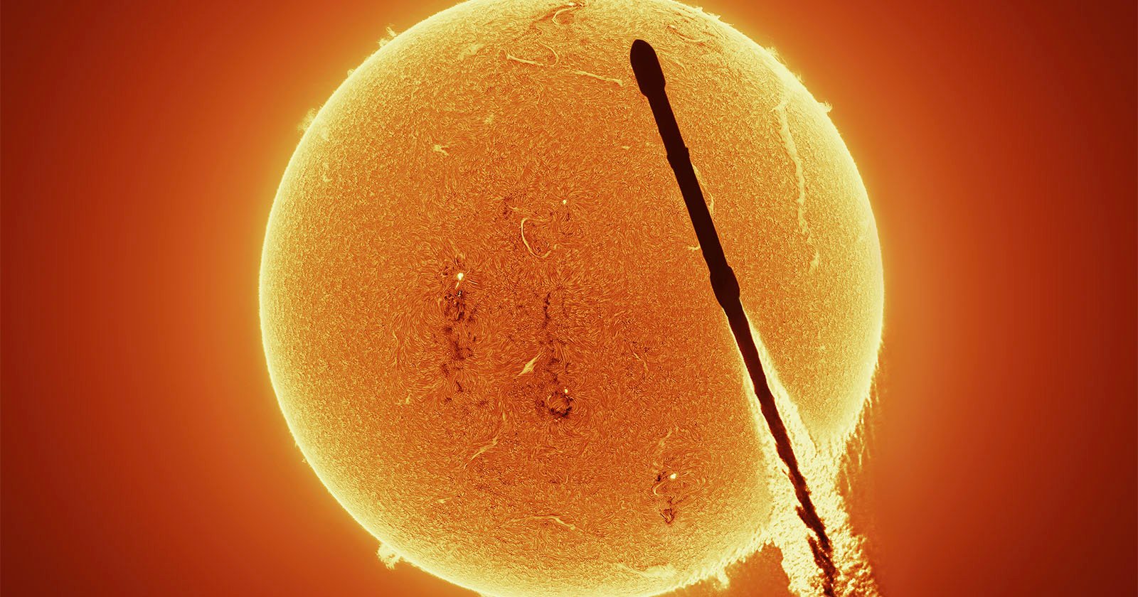 A dark silhouette of a rocket passing in front of the bright, detailed surface of the Sun, with visible solar activity and glowing orange plasma.
