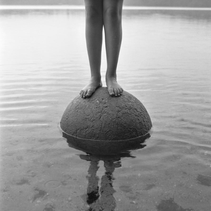 A photo of a man standing on a rock in a body of water