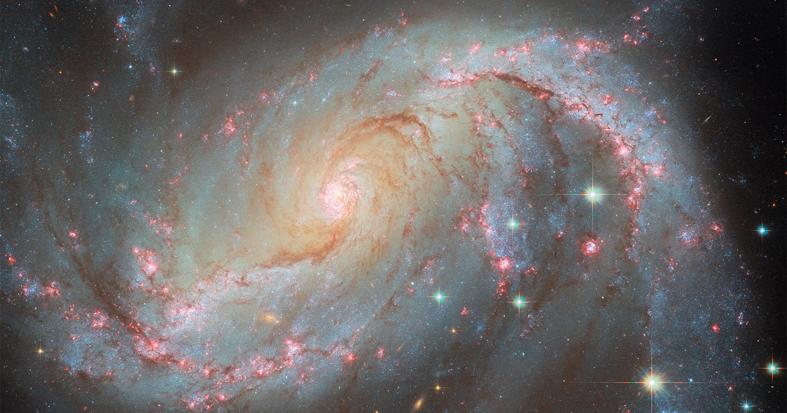 A vivid spiral galaxy with glowing arms extends outward, showcasing bright stars and clusters of pinkish-red nebulas against a dark space backdrop. The galaxy's spiral structure is prominent and intricate.