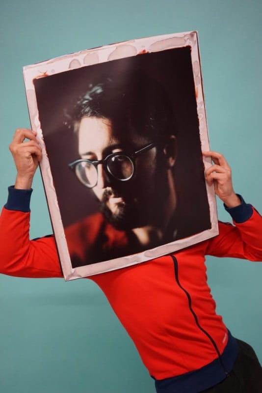 A man holding a giant 20 by 24 inch portrait of his face