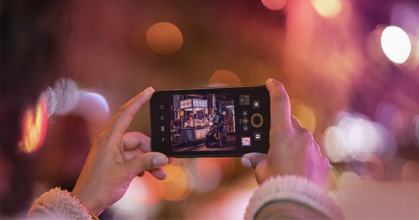 A person taking a photo with their smartphone of a street vendor at night, as seen on the phone's screen, amidst a blur of city lights.