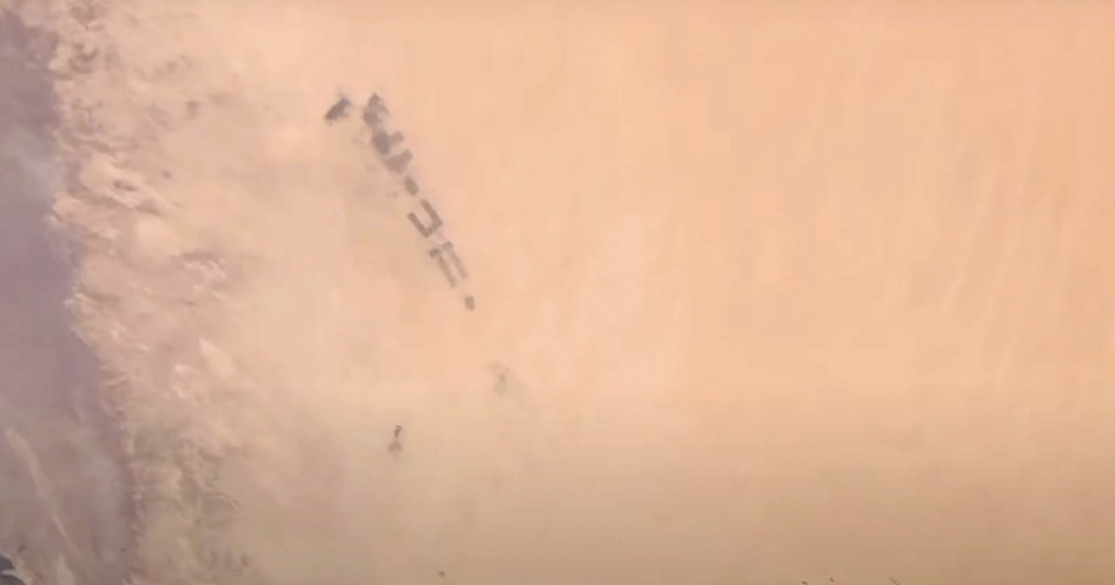 A group of military vehicles moving through a desert landscape, partially obscured by dense clouds of sand and dust.