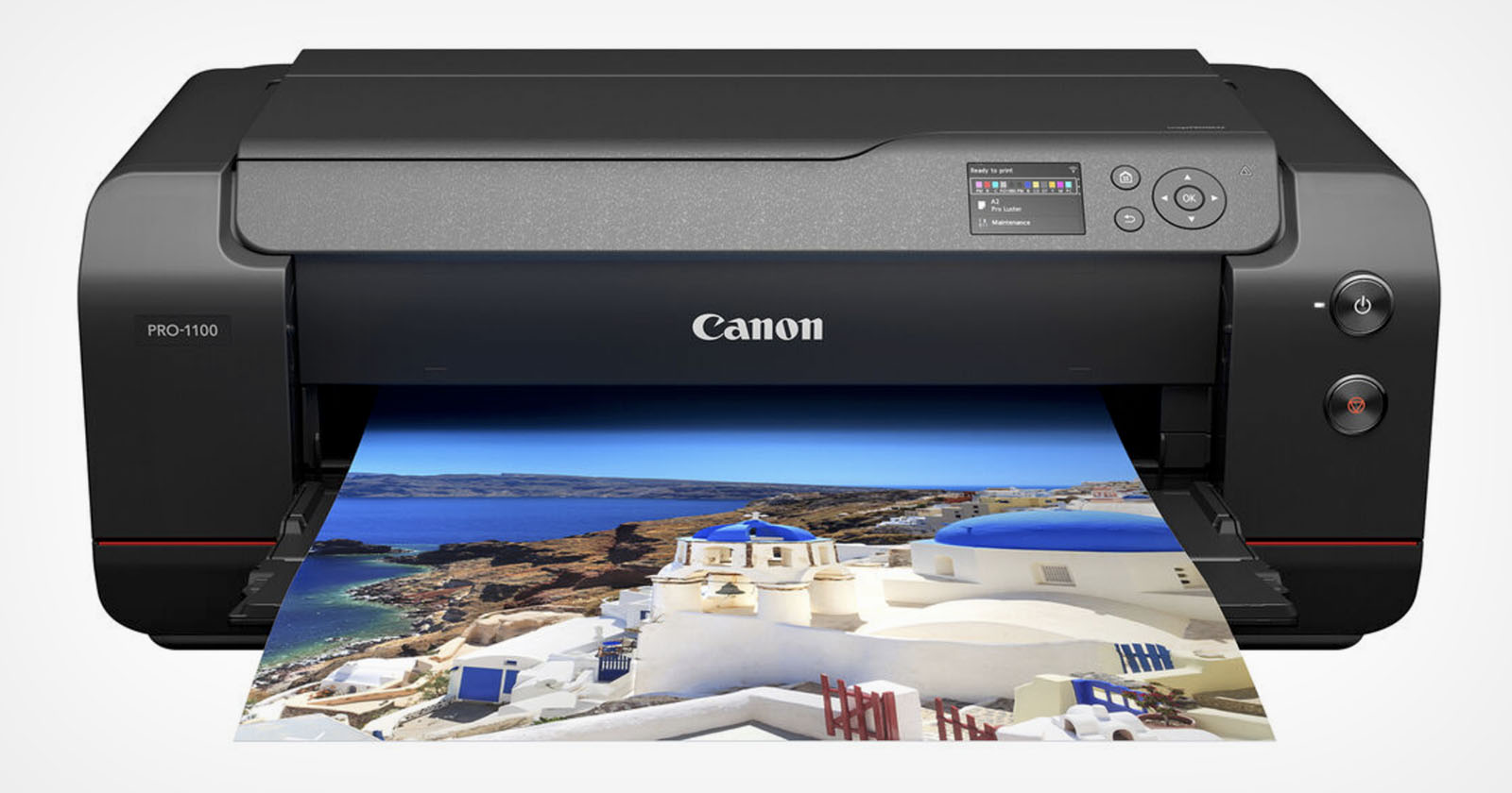 A black Canon PRO-1000 printer on a white background is printing a vibrant photo of a coastal Mediterranean village with white buildings and blue roofs against a backdrop of the sea and sky.