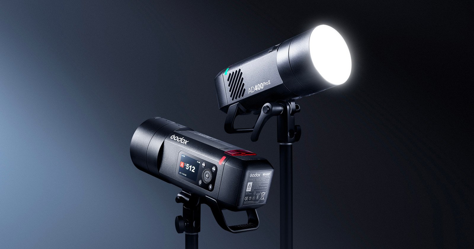 Two professional studio lights on stands, one facing forward with its bright LED illuminated and the other showing its digital display screen and control buttons, both set against a dark gradient background.