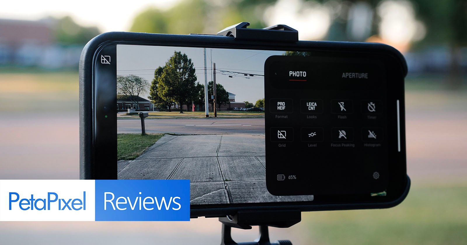 A smartphone mounted on a tripod, displaying a camera app interface with various settings visible. The phone screen shows a clear outdoor scene of a sidewalk, street, and trees in the background. PetaPixel Reviews text is overlayed at the bottom of the image.