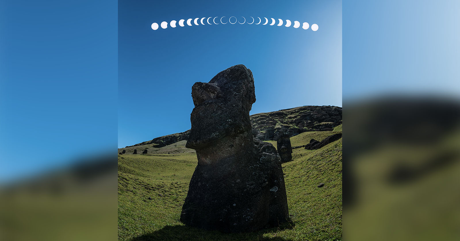 A large stone statue stands on a grassy hill under a clear blue sky. Above the statue, a sequence of moon phases is displayed in a curved line from left to right.