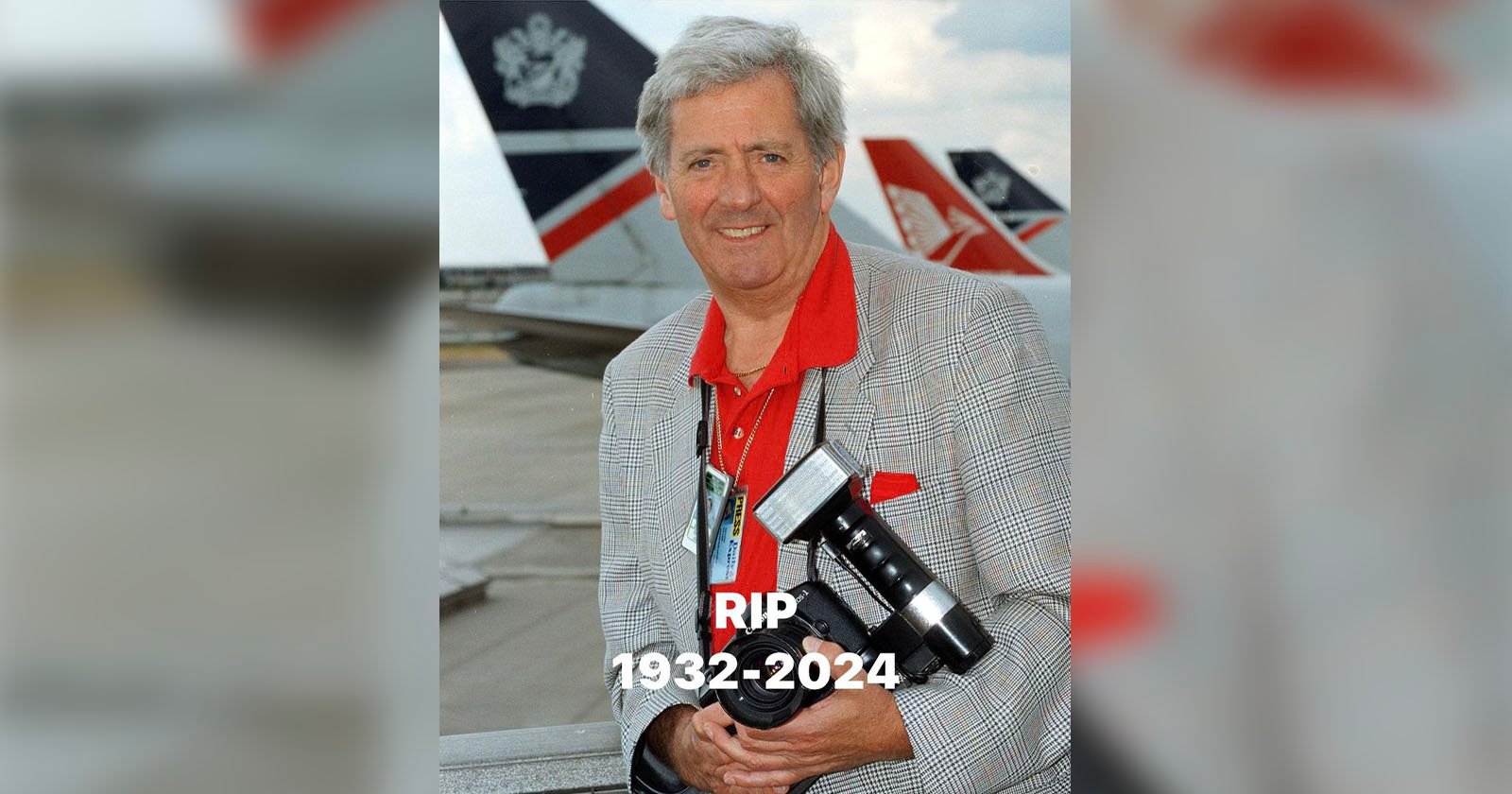 Older man smiling while holding a camera at an airport with airplanes in the background. He is wearing a gray checkered jacket and red shirt. Text below reads RIP 1932-2024.