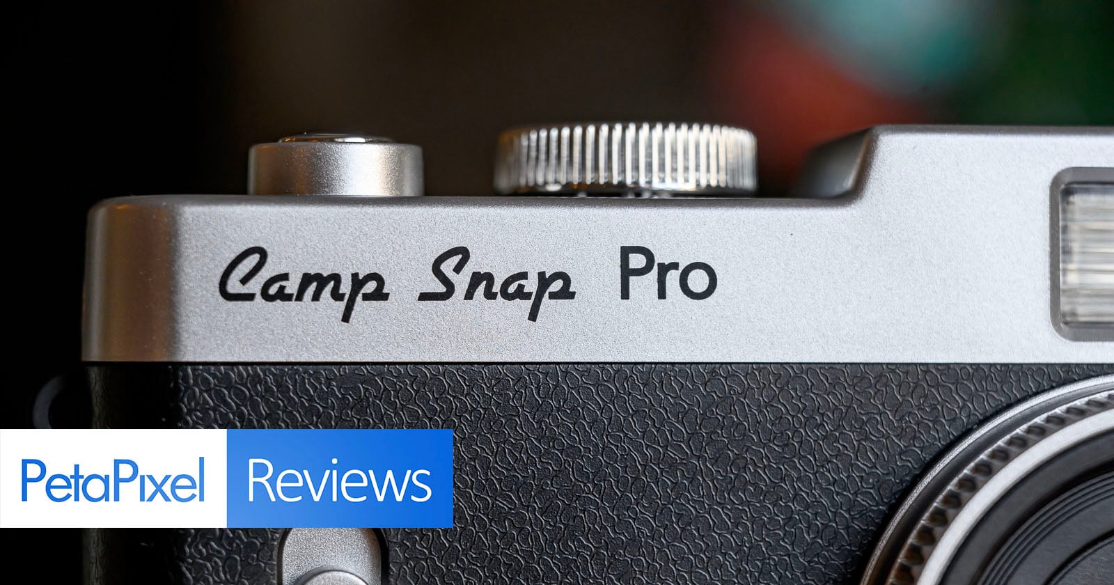 Close-up of a silver and black camera labeled Camp Snap Pro, with a logo in the corner reading PetaPixel Reviews. The focus is on the camera's branding and textured surface.