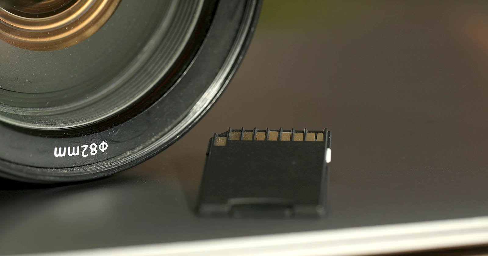 Close-up of a camera lens labeled 82mm next to a black SD memory card resting on a flat, reflective surface.