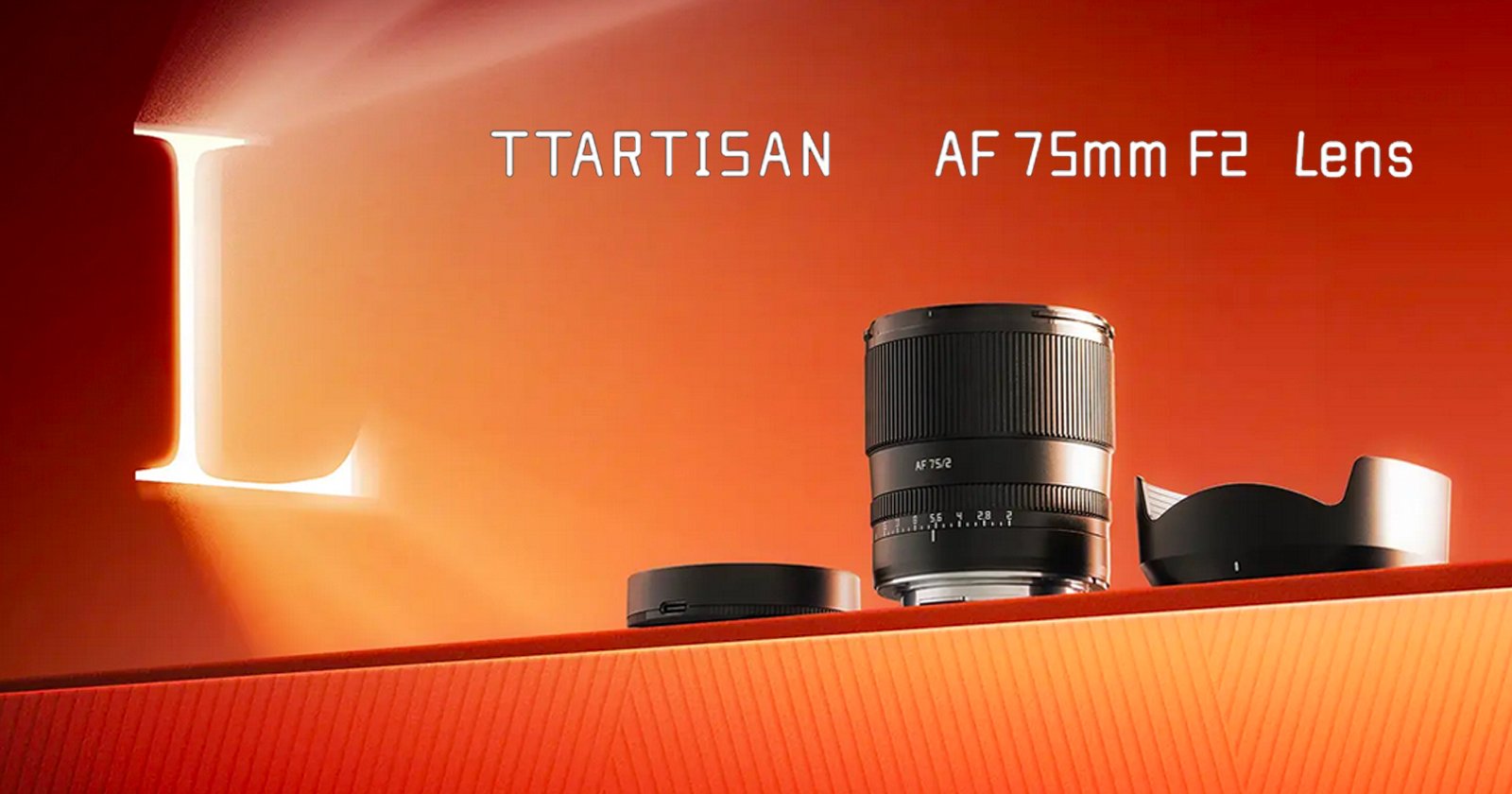 A camera lens is displayed on an orange surface with a lens cap and hood. The text reads TTARTISAN AF 75mm F2 Lens against an orange background with a large illuminated letter L on the left side.