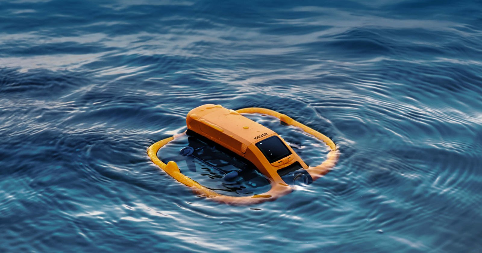 A yellow underwater drone floats on the surface of blue ocean water, surrounded by a yellow ring-shaped flotation device. The device appears to be in operation or testing mode.
