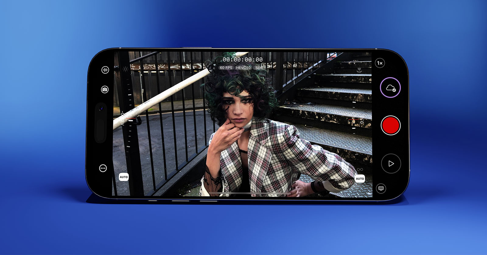 A smartphone displays a photo of a person with curly hair wearing a plaid suit sitting on stairs, looking at the camera. The phone is set against a gradient blue background, and camera app controls are visible on the screen.