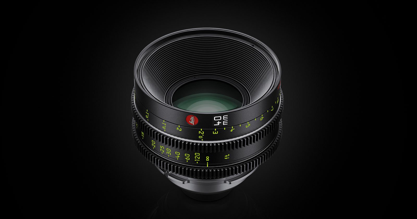 A professional camera lens with ridged focus and aperture rings, marked with white and green numbers, is displayed against a dark background. The lens features a red logo on its barrel.