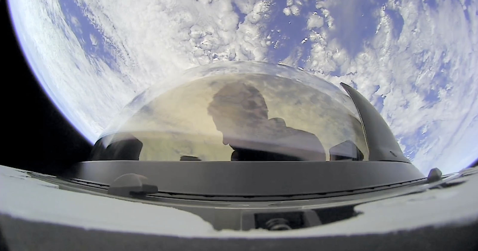 A person is visible through the dome-shaped glass of a spacecraft, with Earth and its cloud formations prominently displayed in the background. The perspective is from space, emphasizing the vastness of the planet below.