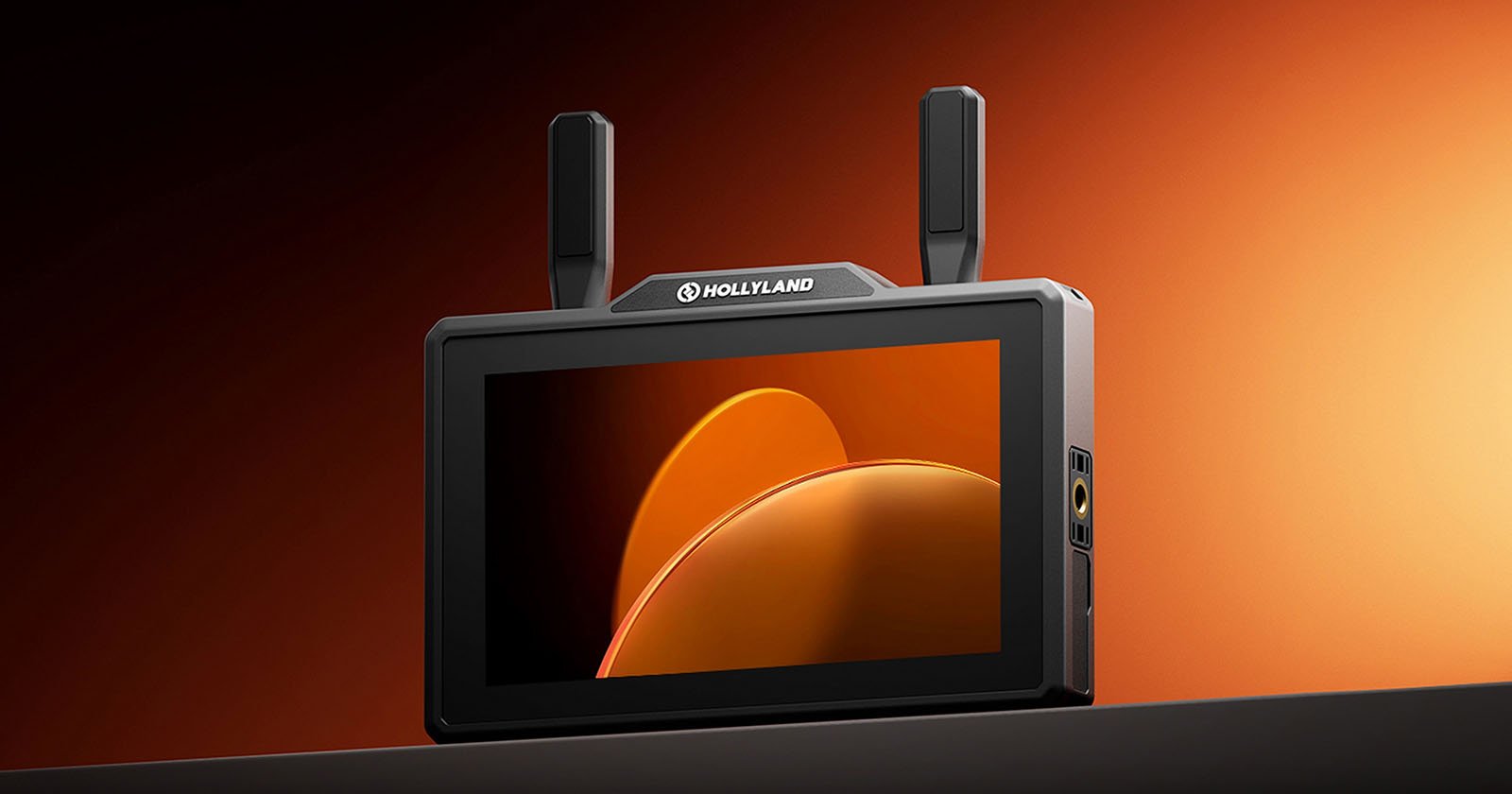 A portable Hollyland monitor with two antennas displays an abstract orange and yellow graphic on its screen, set against an orange gradient background.